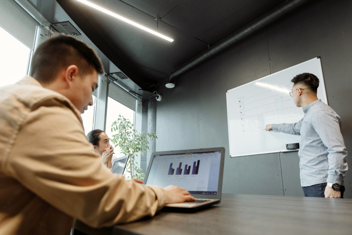 Accountants in Sydney discussing financial performance during a strategy meeting, with one presenting data on a whiteboard and another reviewing figures on a laptop.