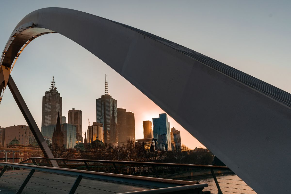 Melbourne skyline at sunset framed by an arched footbridge over the Yarra River