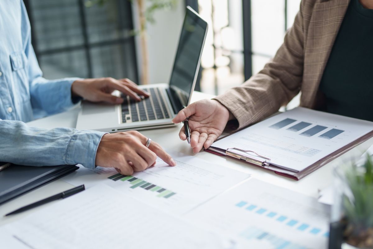two business people sitting at a table with papers and a laptop